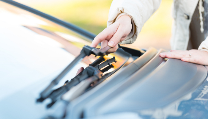 Woman picking up windshield wiper of a black car to change its blades